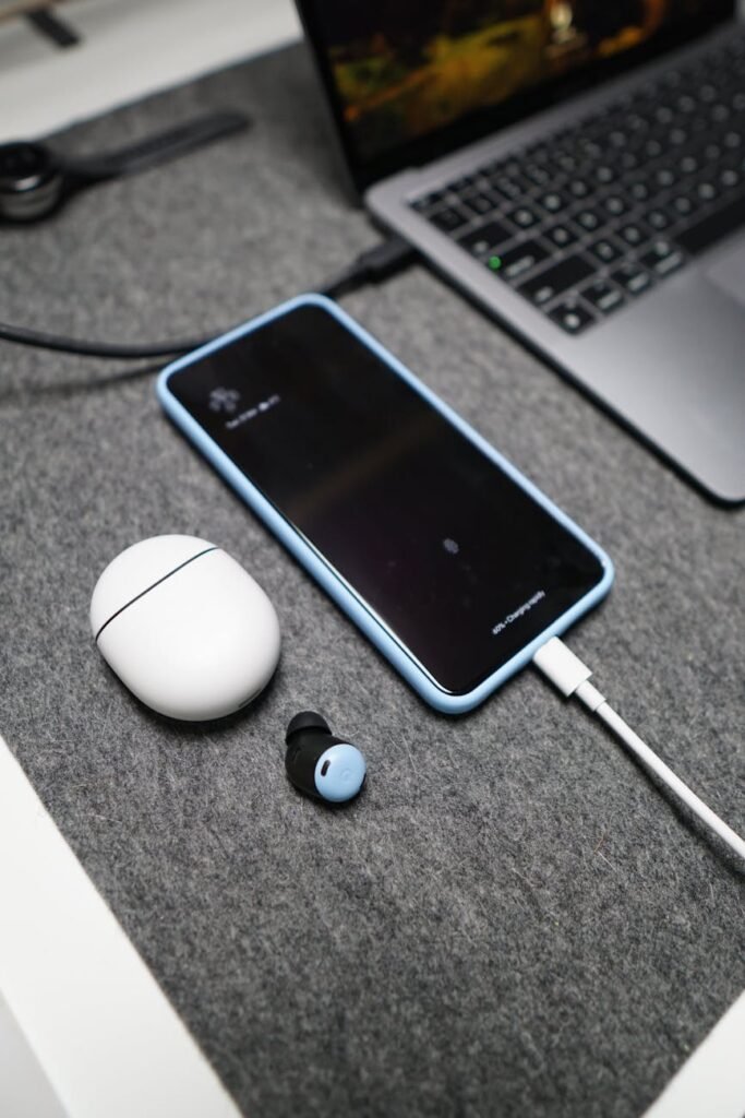 charging smartphone and wireless earphones on the desk next to the laptop